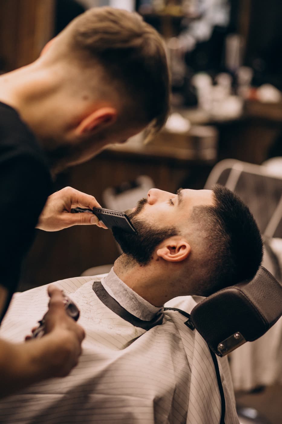 Un barbero perfilando la barba a un cliente en su silla.